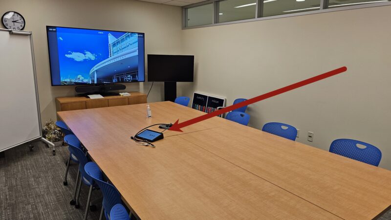 Picture of a medium conference room in building E52 pointing to the Zoom Room Controller touchpanel on the table